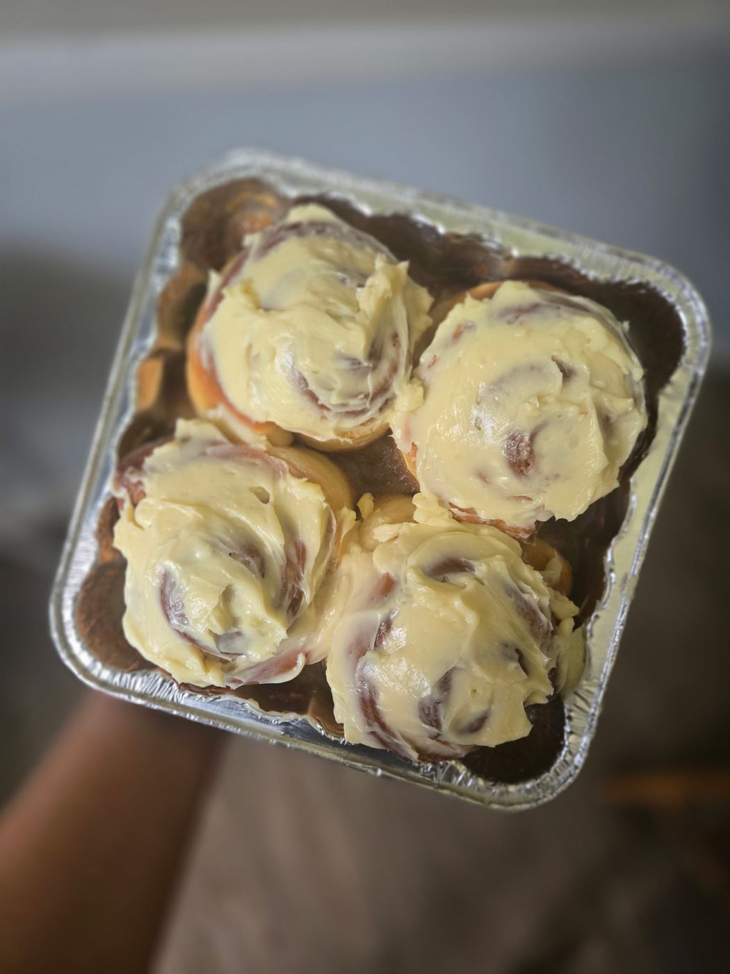 Four soft cinnamon rolls topped with buttercream icing in a foil pan